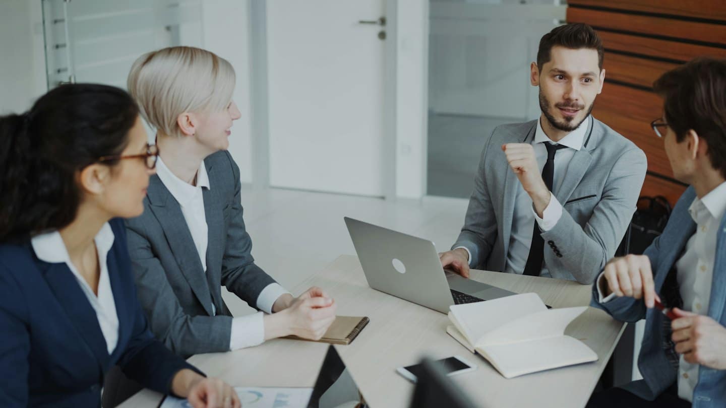 Des professionnels discutent affaires autour d'une table de conférence avec des ordinateurs portables et des documents.
